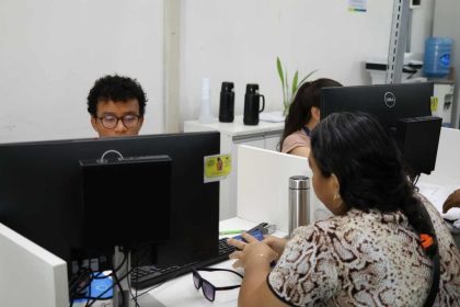 Pessoas trabalhando em escritório com computadores, possivelmente em processo seletivo ou prestando atendimento.