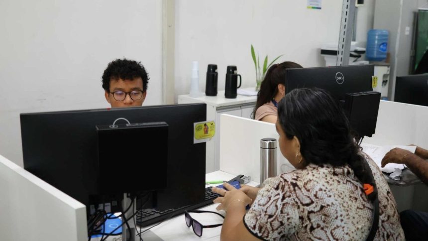 Pessoas trabalhando em escritório com computadores, possivelmente em processo seletivo ou prestando atendimento.