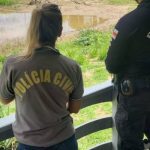 Policiais civis em local de investigação próximo a rio.