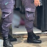 Policial investigando cena de crime em Manaus, com pessoa caída no chão.