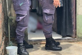 Policial investigando cena de crime em Manaus, com pessoa caída no chão.