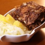 Prato de carne de porco com acompanhamentos em tigela branca.