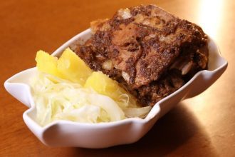 Prato de carne de porco com acompanhamentos em tigela branca.