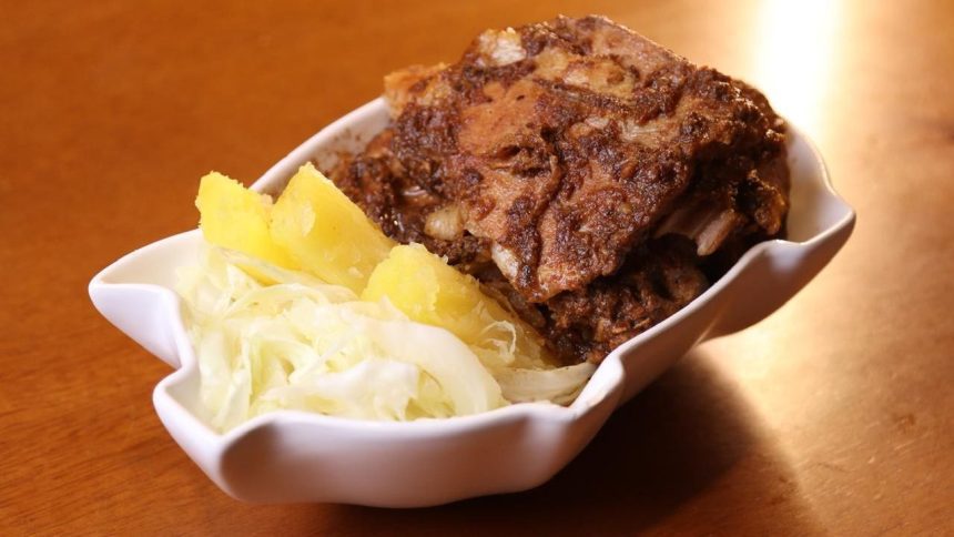 Prato de carne de porco com acompanhamentos em tigela branca.