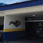 Prédio da DECCM Norte/Leste em Manaus, com carro da polícia e frase 'Atendimento Integrado à Mulher'.