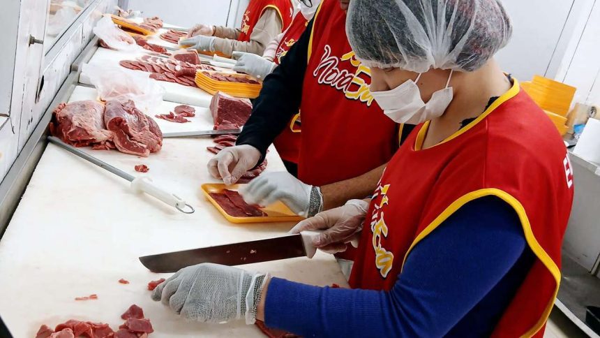 Profissionais preparando carne em açougue, com aventais e toucas.