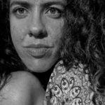 Retrato em preto e branco de uma mulher com cabelo encaracolado e um olhar sério.