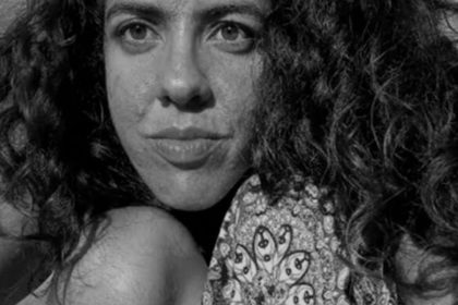 Retrato em preto e branco de uma mulher com cabelo encaracolado e um olhar sério.