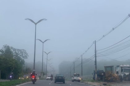 Rodovia com neblina em Manaus, com veículos em movimento e postes de iluminação.