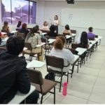 Sala de aula com estudantes e palestrante, possível apresentação sobre concurso.