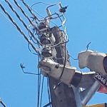 Técnico trabalhando em poste de energia elétrica com fios danificados e equipamento de proteção.