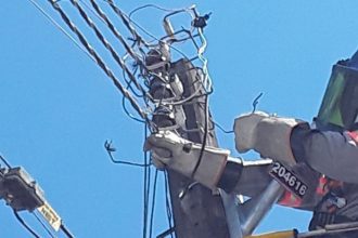 Técnico trabalhando em poste de energia elétrica com fios danificados e equipamento de proteção.