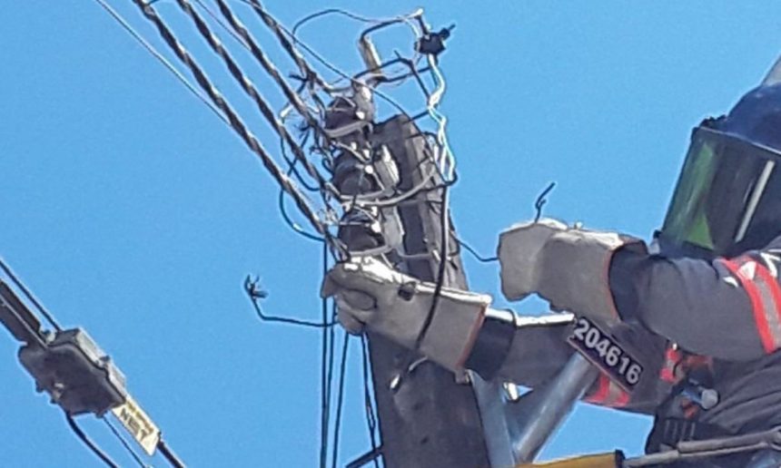 Técnico trabalhando em poste de energia elétrica com fios danificados e equipamento de proteção.