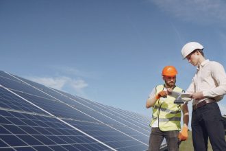Técnicos analisando painéis solares em instalação, sob céu azul.