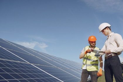 Técnicos analisando painéis solares em instalação, sob céu azul.