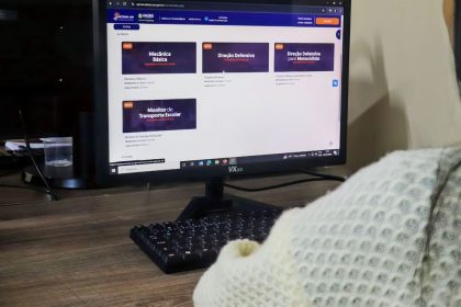 Tela de computador mostra cursos de trânsito online: Mecânica Básica, Direção Defensiva e Monitor de Transporte Escolar.