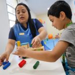 Terapeuta e criança brincando com brinquedos educativos em sala de aula.