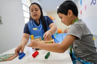 Terapeuta e criança brincando com brinquedos educativos em sala de aula.