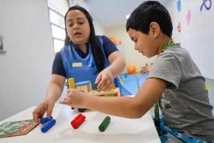 Terapeuta e criança brincando com brinquedos educativos em sala de aula.