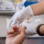 Teste de sangue para sífilis em jovem adulto. Profissional com luvas coleta amostra.