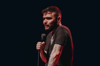 Tiago Santineli segurando um microfone em um palco escuro