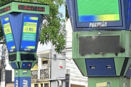 Totem de reconhecimento facial pichado em praça, exibindo mensagens.