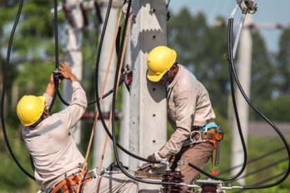 Trabalhadores da rede elétrica usando equipamentos de proteção individual (EPIs) em poste de energia.