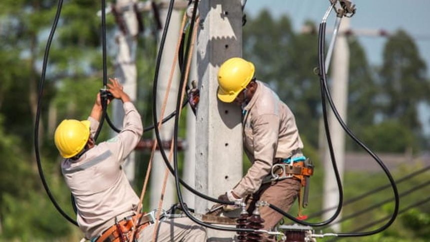 Trabalhadores da rede elétrica usando equipamentos de proteção individual (EPIs) em poste de energia.