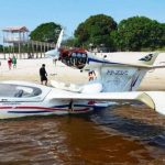 Ultraleve acidentado em praia do Rio Andirá, Amazonas, com pessoas ao redor.