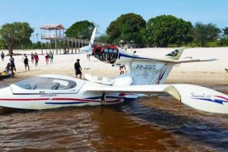 Ultraleve acidentado em praia do Rio Andirá, Amazonas, com pessoas ao redor.