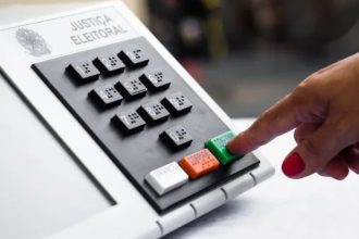 Urna eletrônica com dedo pressionando o botão de confirmação, simbolizando votação.