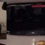 Veículo branco com danos na lataria e pneu, possivelmente após ataque.