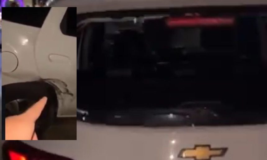 Veículo branco com danos na lataria e pneu, possivelmente após ataque.