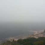 Vista panorâmica da costa do Amazonas sob forte névoa, com vegetação exuberante e mar agitado.