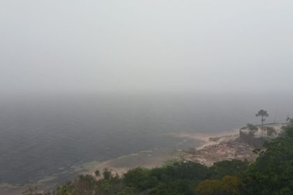Vista panorâmica da costa do Amazonas sob forte névoa, com vegetação exuberante e mar agitado.