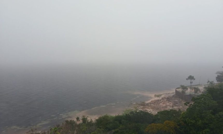 Vista panorâmica da costa do Amazonas sob forte névoa, com vegetação exuberante e mar agitado.