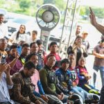 Governador Wilson Lima discursa para multidão em evento ao ar livre, com pessoas registrando com celulares.