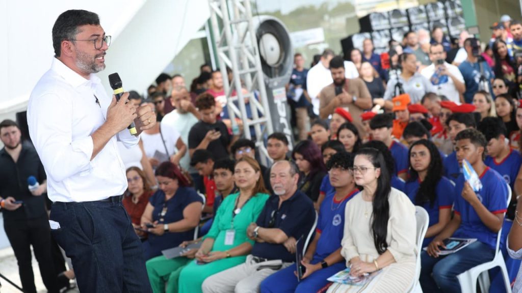 Governador Wilson Lima discursa para multidão em evento ao ar livre, com pessoas registrando com celulares.