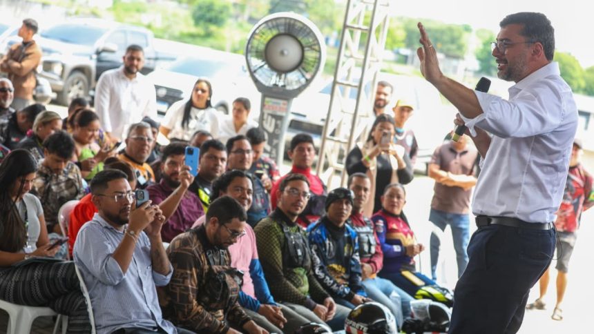 Governador Wilson Lima discursa para multidão em evento ao ar livre, com pessoas registrando com celulares.