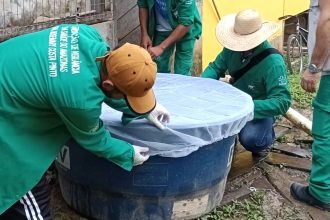 Profissionais inspecionando reservatório de água com rede de proteção, ação de combate a arboviroses no Amazonas.