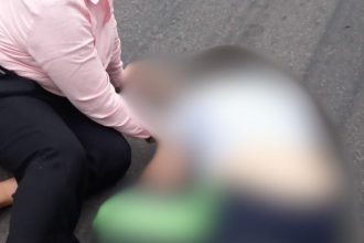 Acidente no Distrito Industrial: pessoa caída com roupa rosa e preta, com outra pessoa desfocada.