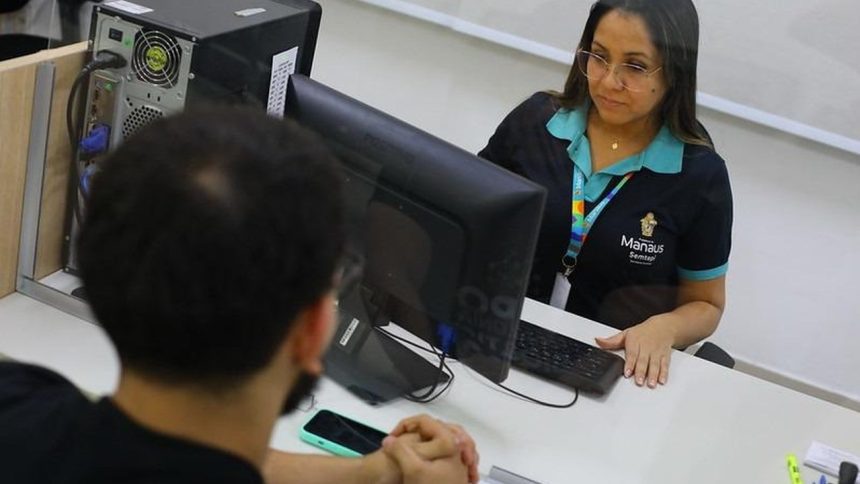Atendente do Sine Manaus auxiliando cliente em frente a computador.