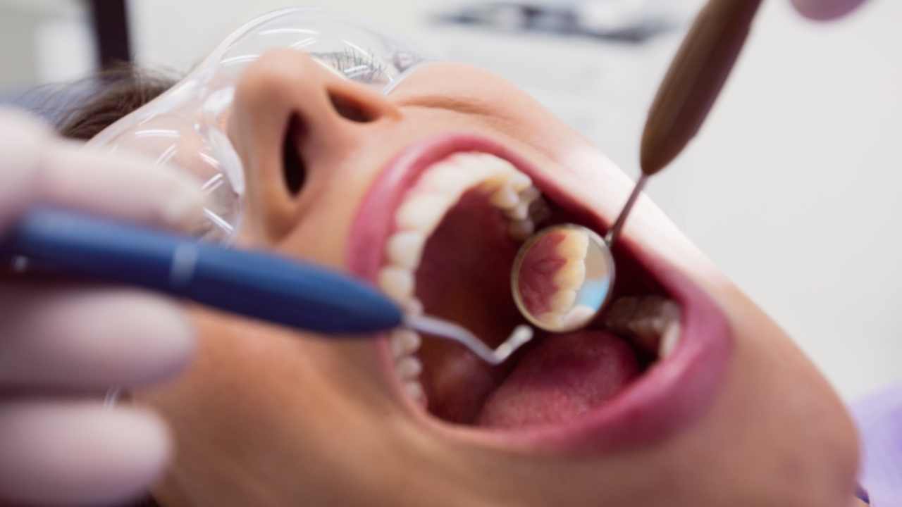 Dentista examinando a boca de um paciente com instrumentos odontológicos, usando um espelho.