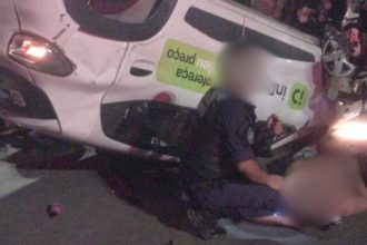 Carro de aplicativo capotado na Zona Leste de Manaus após acidente, com pessoas feridas e policial no local.