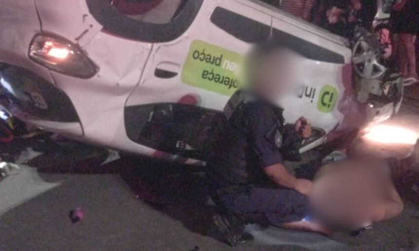 Carro de aplicativo capotado na Zona Leste de Manaus após acidente, com pessoas feridas e policial no local.