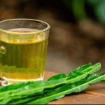 Chá de carqueja em copo de vidro com folhas verdes ao lado, em fundo desfocado. Ieal para eliminar a gordura no fígado