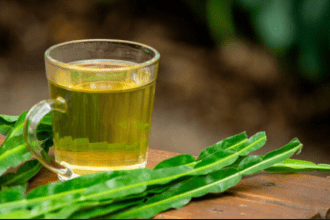 Chá de carqueja em copo de vidro com folhas verdes ao lado, em fundo desfocado. Ieal para eliminar a gordura no fígado