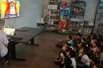 Crianças assistem a filme "Cine Mitos da Amazônia" em sala de aula.