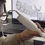 Dentista usando scanner intraoral para digitalizar um molde dentário e analisar em um computador.