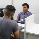 Dois homens em um escritório do Sine em Manaus, um atendendo e outro sendo atendido.